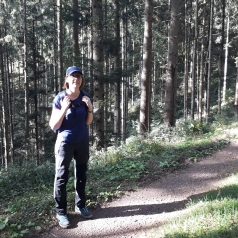 Marie face caméra sur un sentier, des sapins tout autour