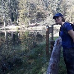 Marie à côté du panneau désignant l'Etang du Coucou, et un bout dudit étang où les arbres de la rive se reflètent