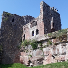 Un château en ruines percé de fenêtres gothiques. Les pierres sont roses et le mur encore très haut